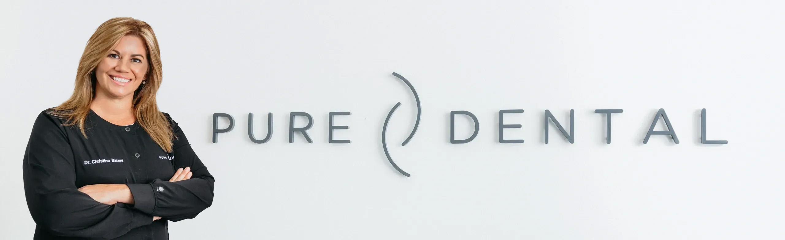 Pure Dental Logo with Dr. Christine Baroni standing in front of it.